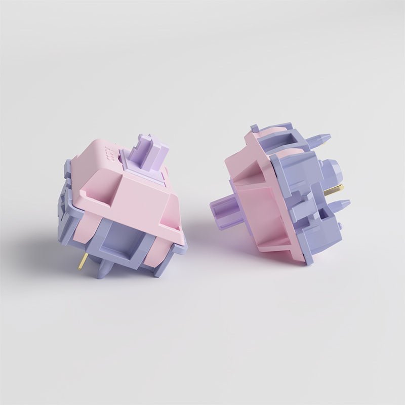 Mechanical keyboard switch, two angles showing pastel pink and lavender parts with gold pins