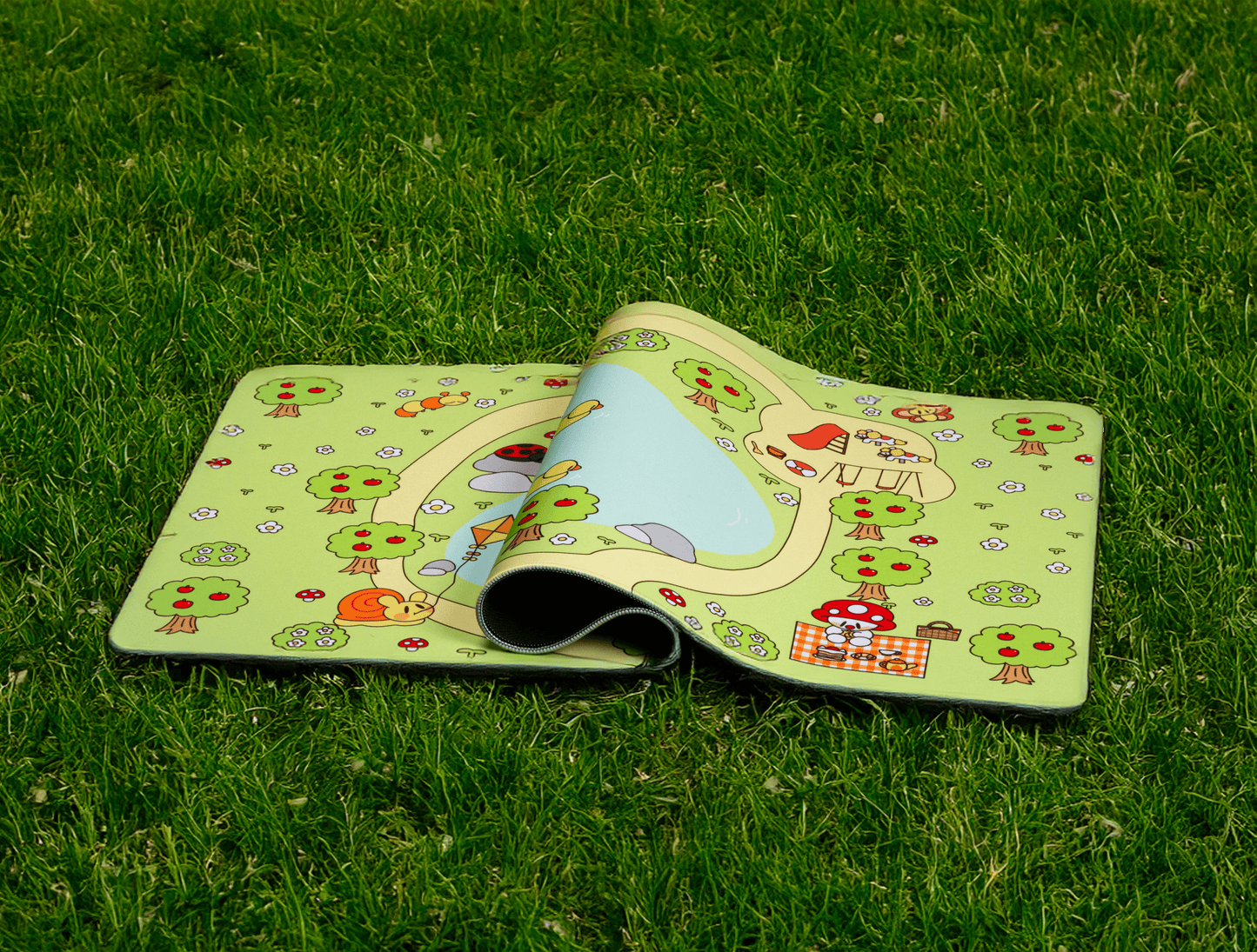 Picnic desk mat rolled and partially open on grass, showing picnic characters and border