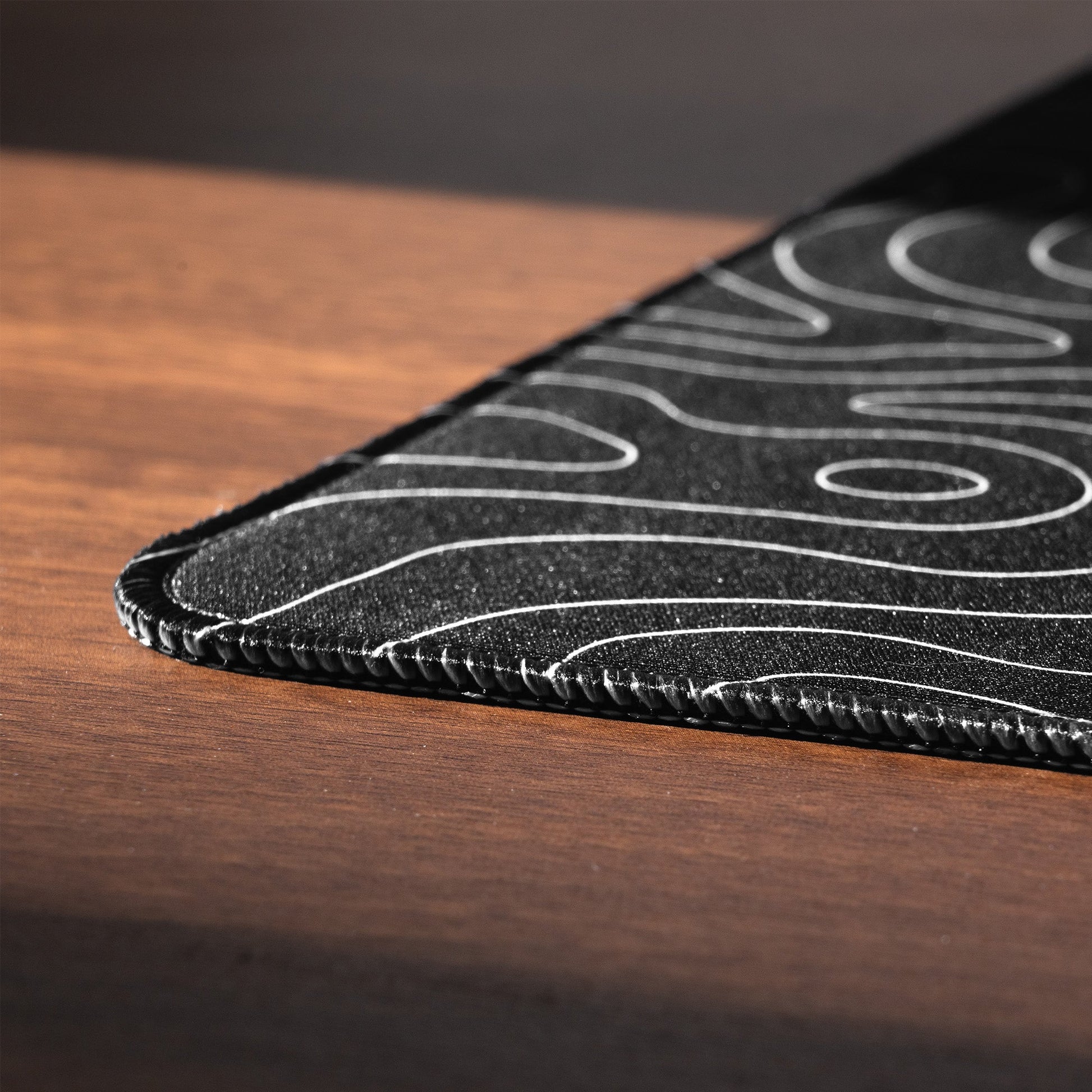 Close-up of desk mat edge with topographic lines and double stitched border.
