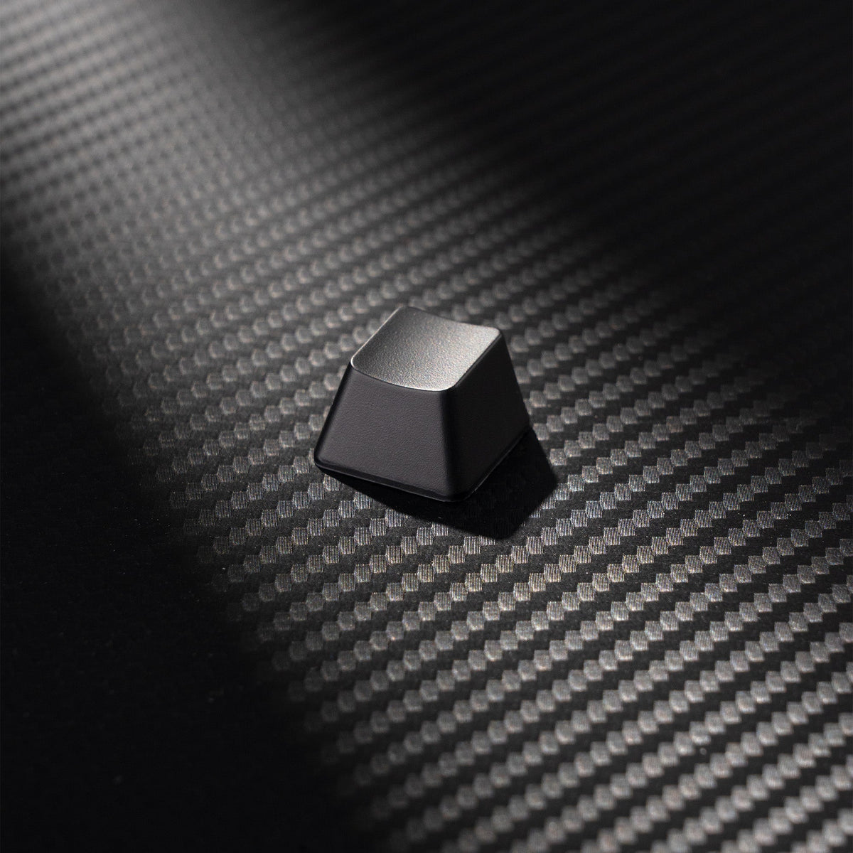 Matte dark keycap with subtle highlights on textured carbon-fiber style surface
