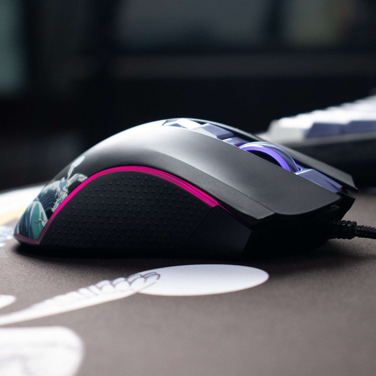 Black wired gaming mouse with textured grip and pink LED ring, wave graphic on top.