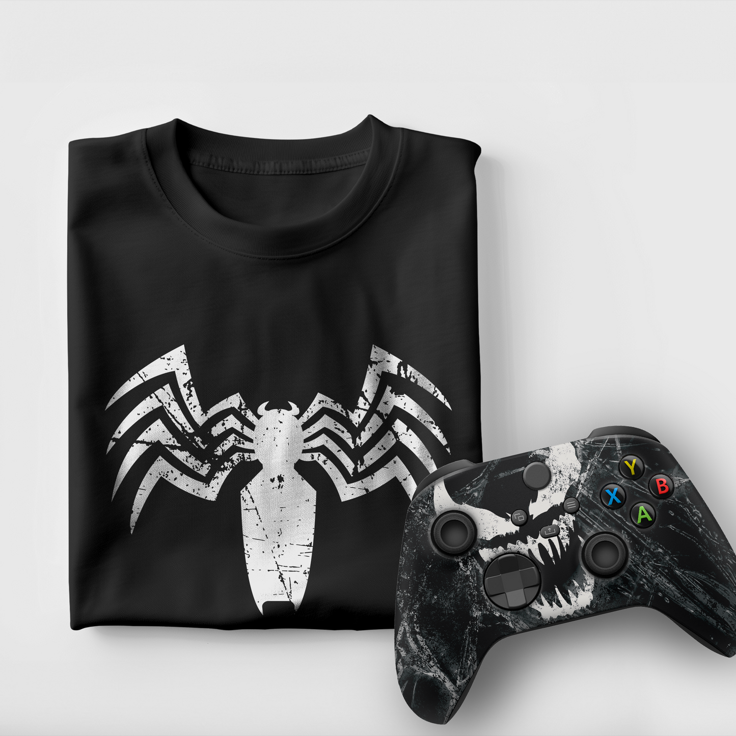 Black graphic T-shirt with white spider emblem; Xbox controller with ABXY buttons