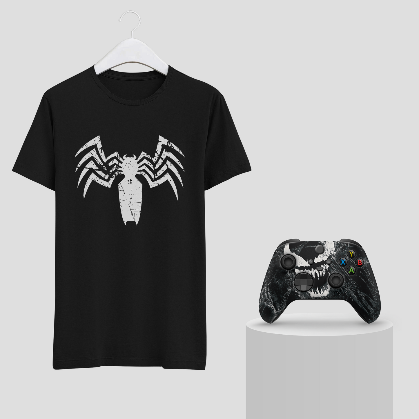 Black graphic T-shirt with white spider emblem on hanger; Xbox controller beside it