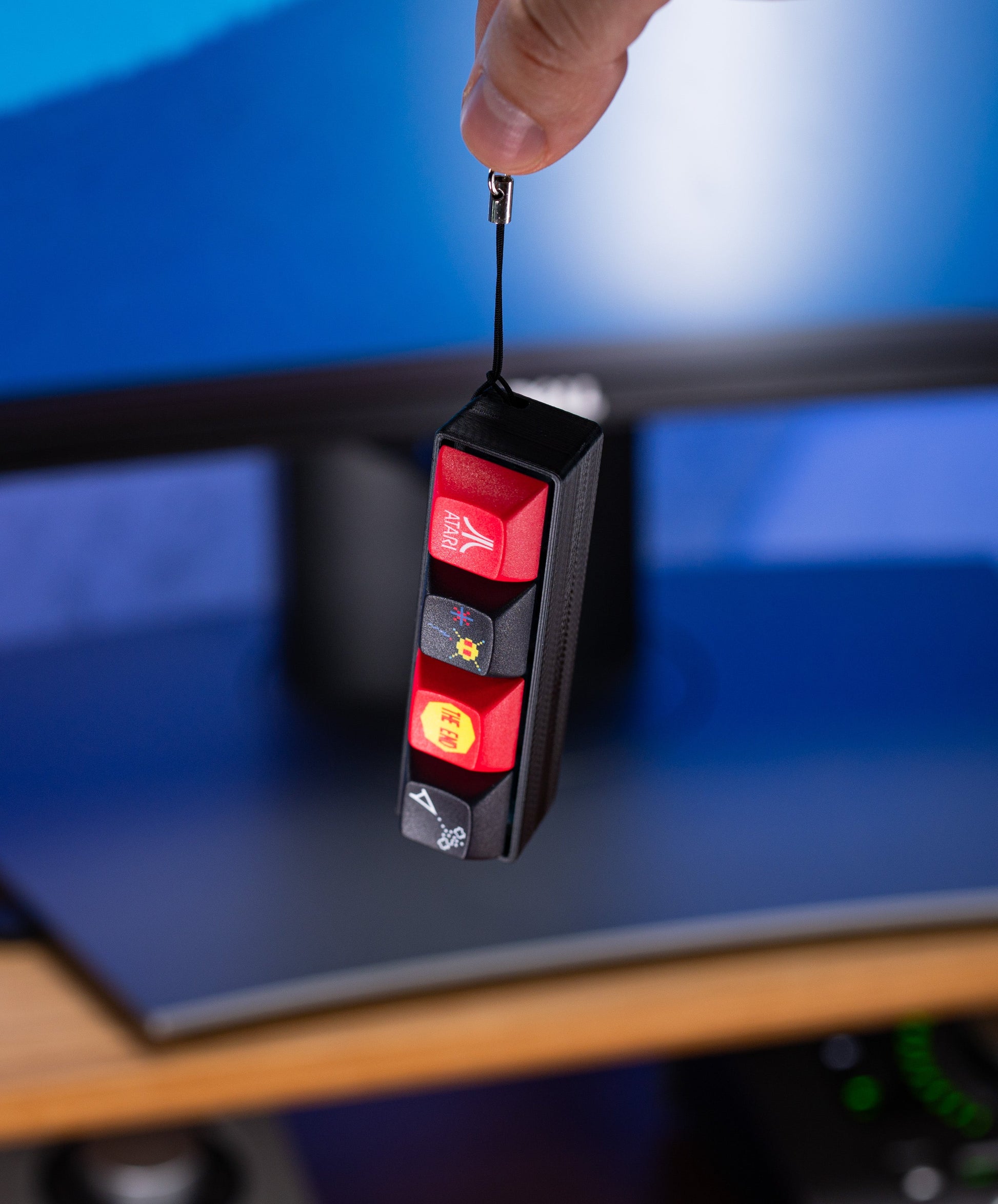 Atari Keycap Fidget held by hand; red keycaps on a black base with keychain