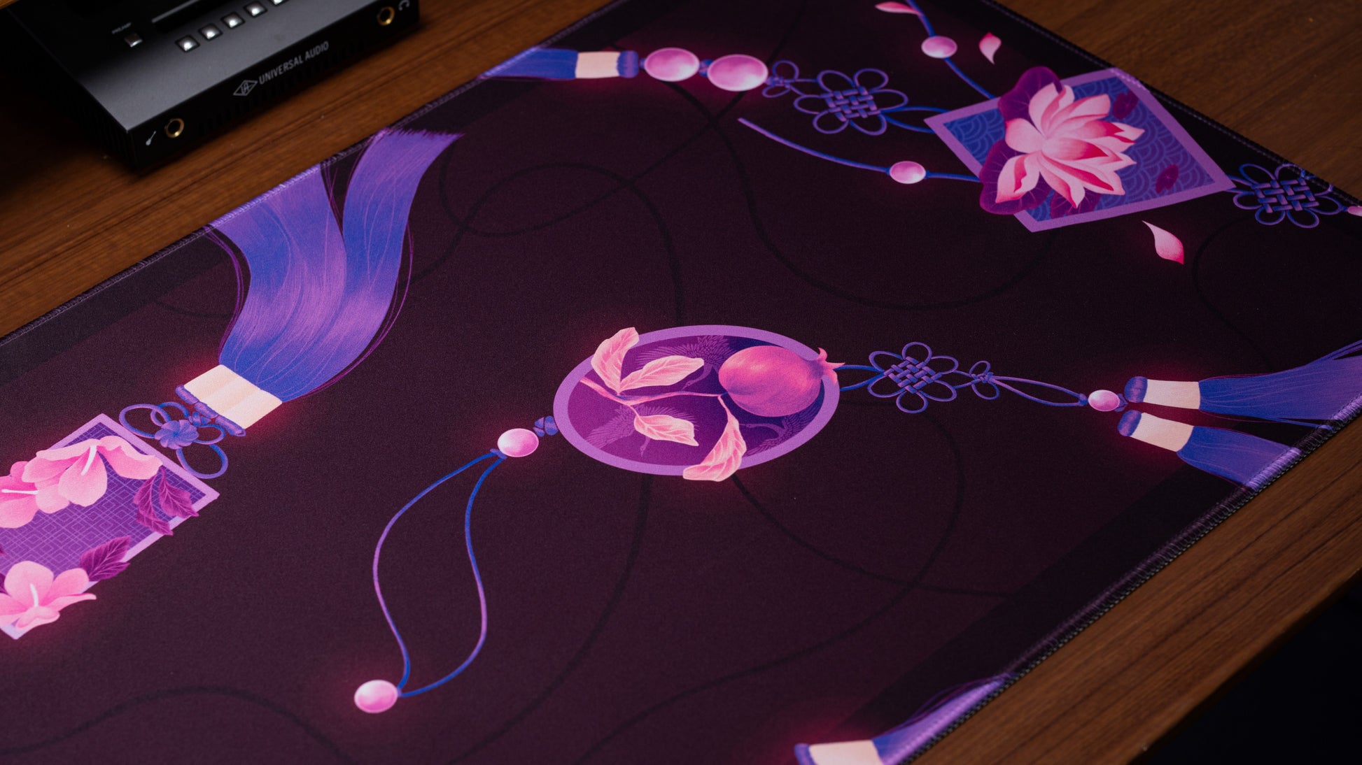 Rectangular desk mat corner close-up with purple ribbon, pink petals, and floral motif