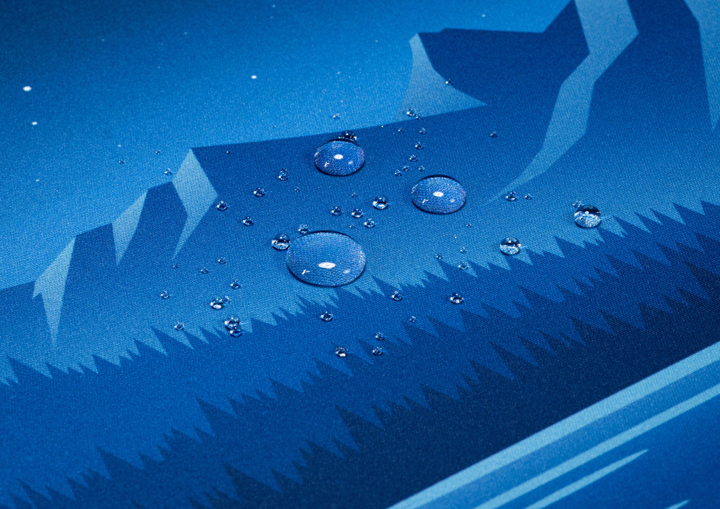 Blue desk mat close-up with water droplets over geometric pine and mountain print