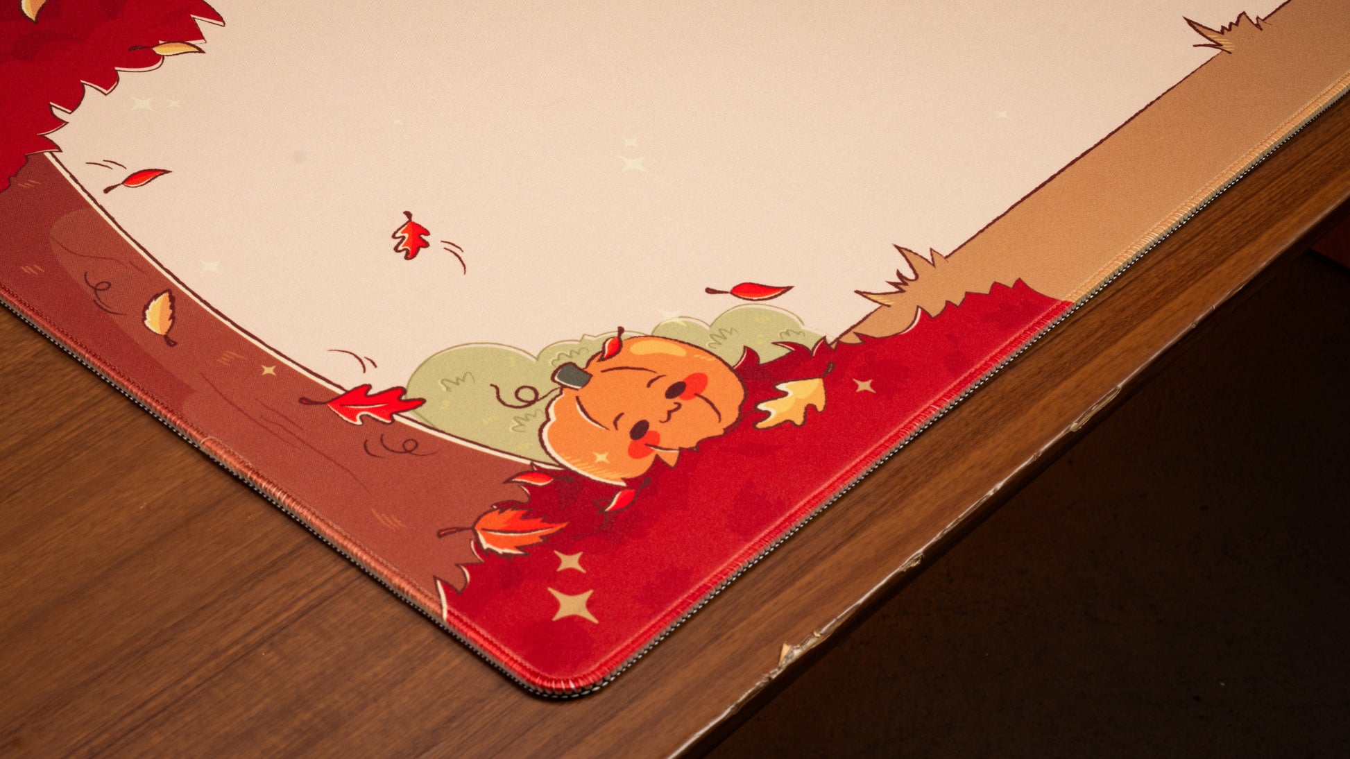 Pumpkin desk mat corner with stitched edge, red base, cream center, smiling pumpkin graphic