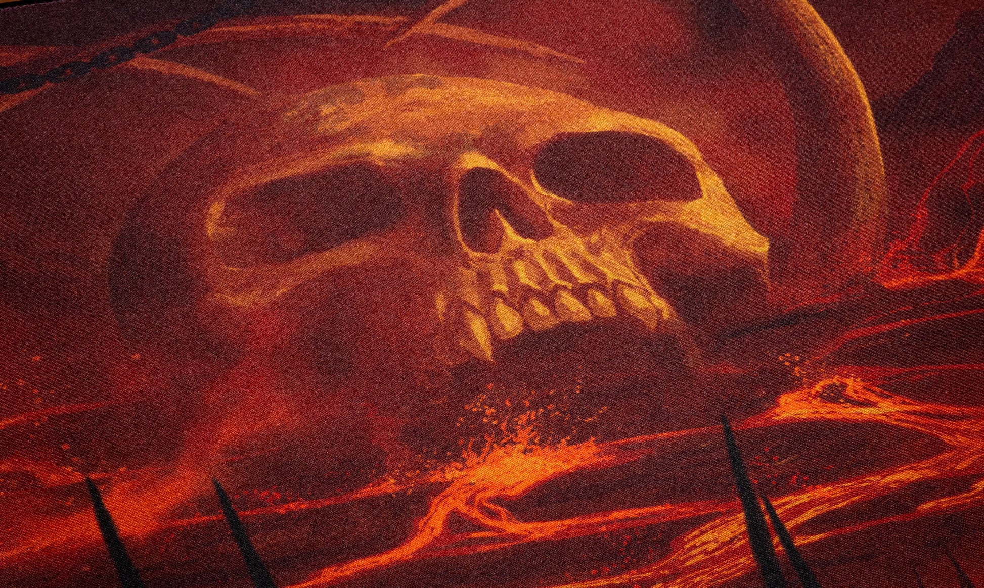 Desk mat close-up graphic of a glowing skull over fiery red clouds and smoke