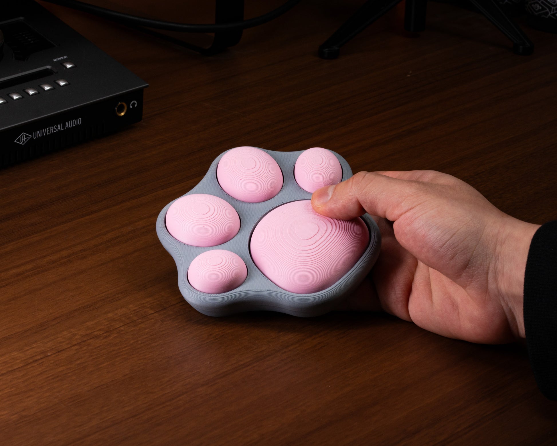 Cat-paw fidget with pink ridged pads on a gray base; hand presses one pad
