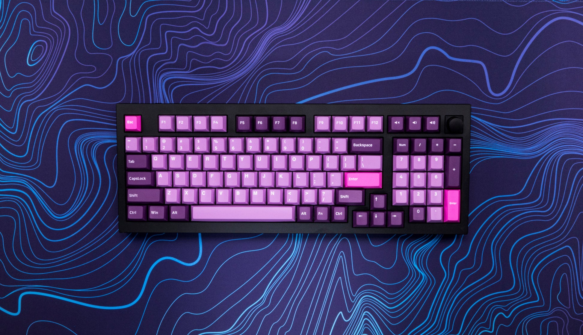 Purple-blue desk mat with blue contour line pattern under an RGB backlit keyboard