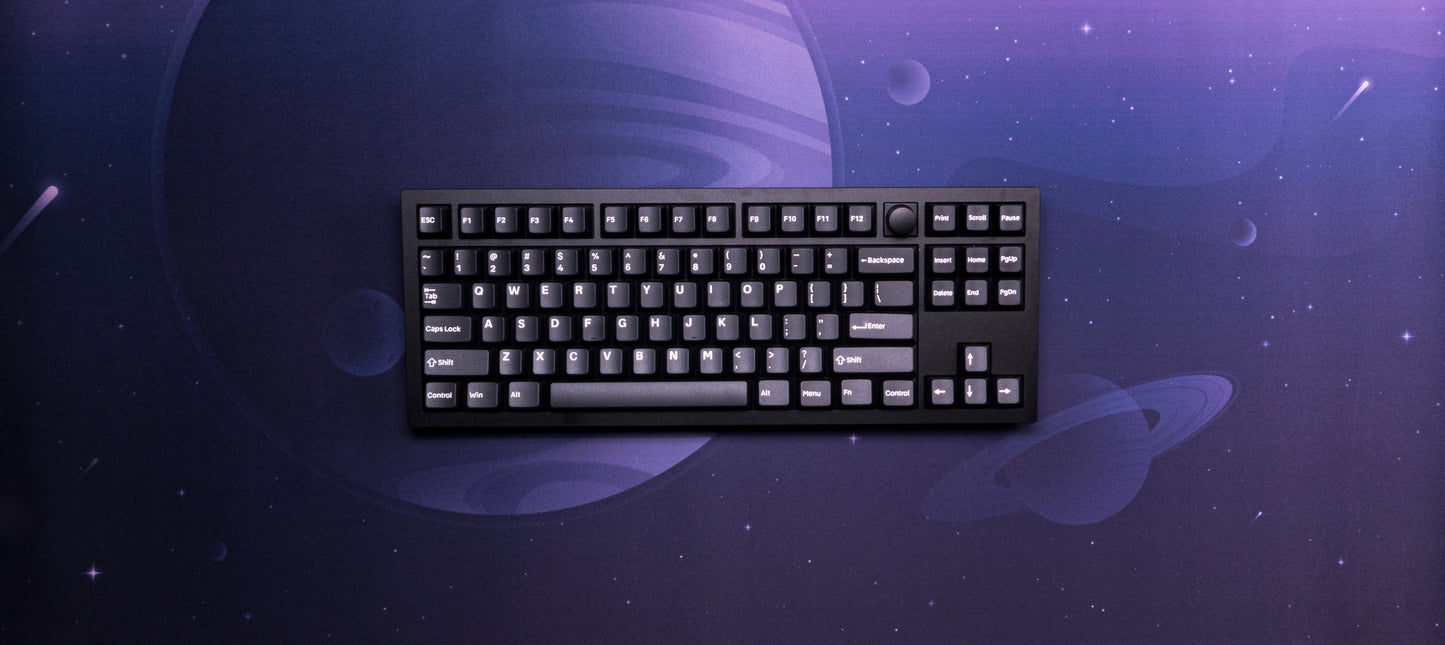 Desk mat with dark purple space print and a black keyboard centered