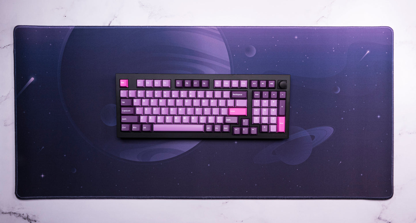 Desk mat with dark purple space print and a keyboard centered on top