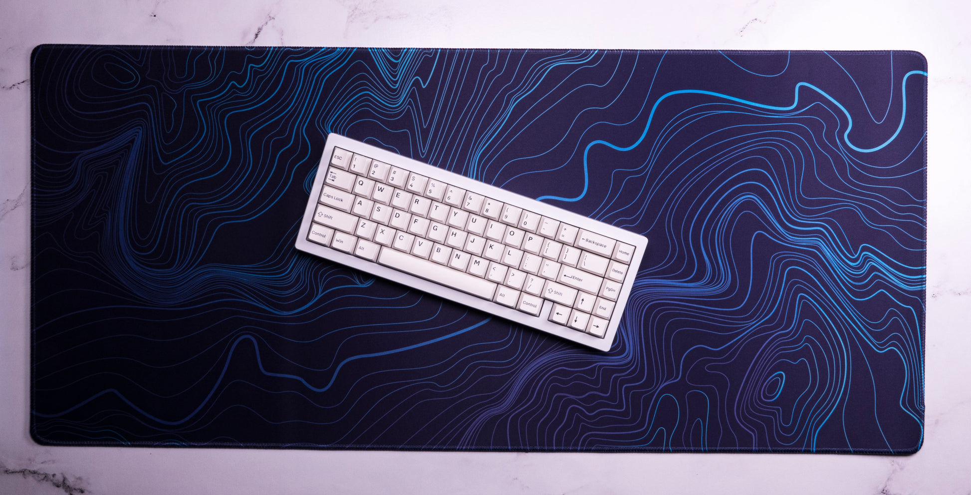 Purple-blue desk mat with blue contour line topographic pattern under a white keyboard