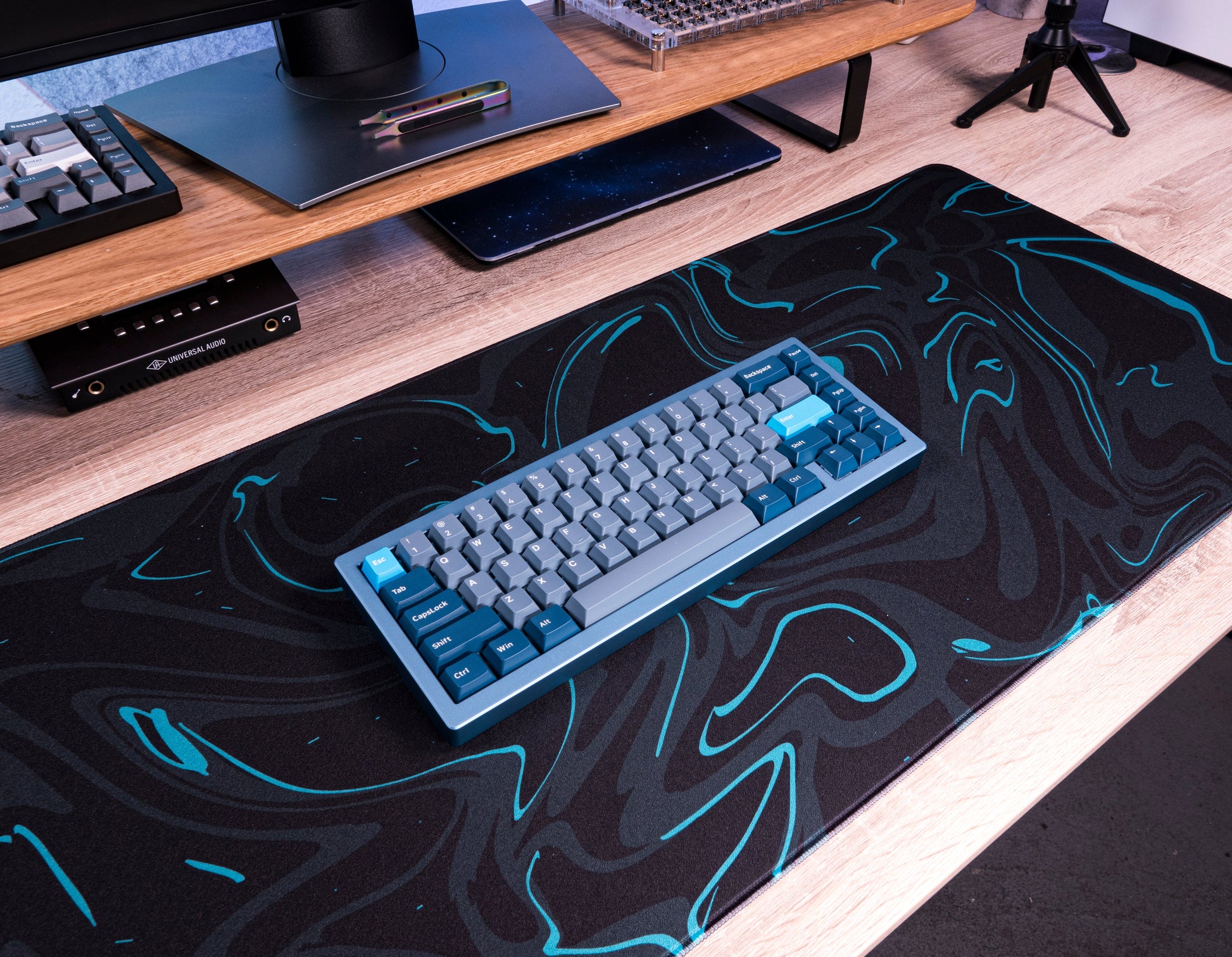 Teal-accented black desk mat with marble swirl pattern under a keyboard