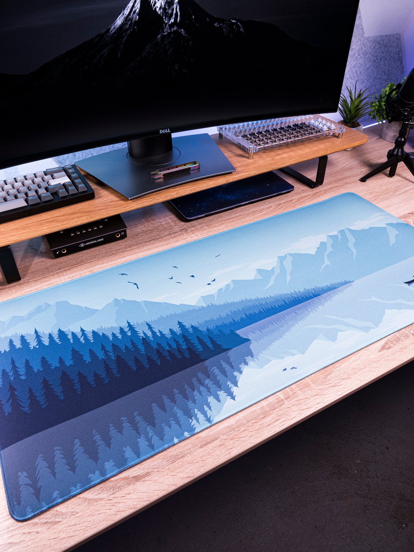 Alberta V2 desk mat with light blue mountain and pine forest print along desk