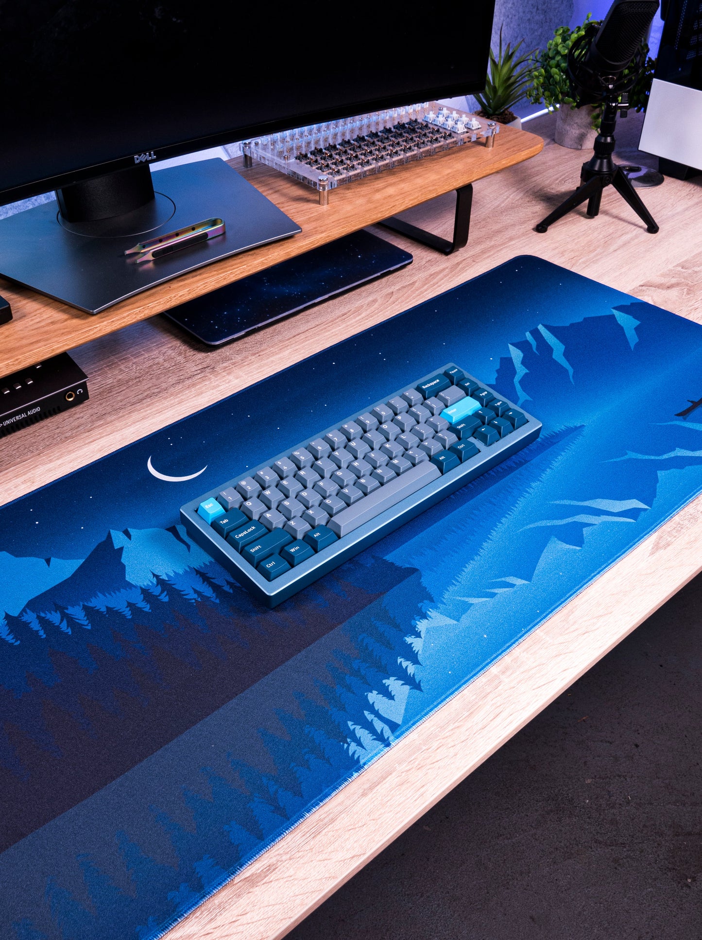 Alberta V2 desk mat with bright blue night forest and mountains pattern near keyboard