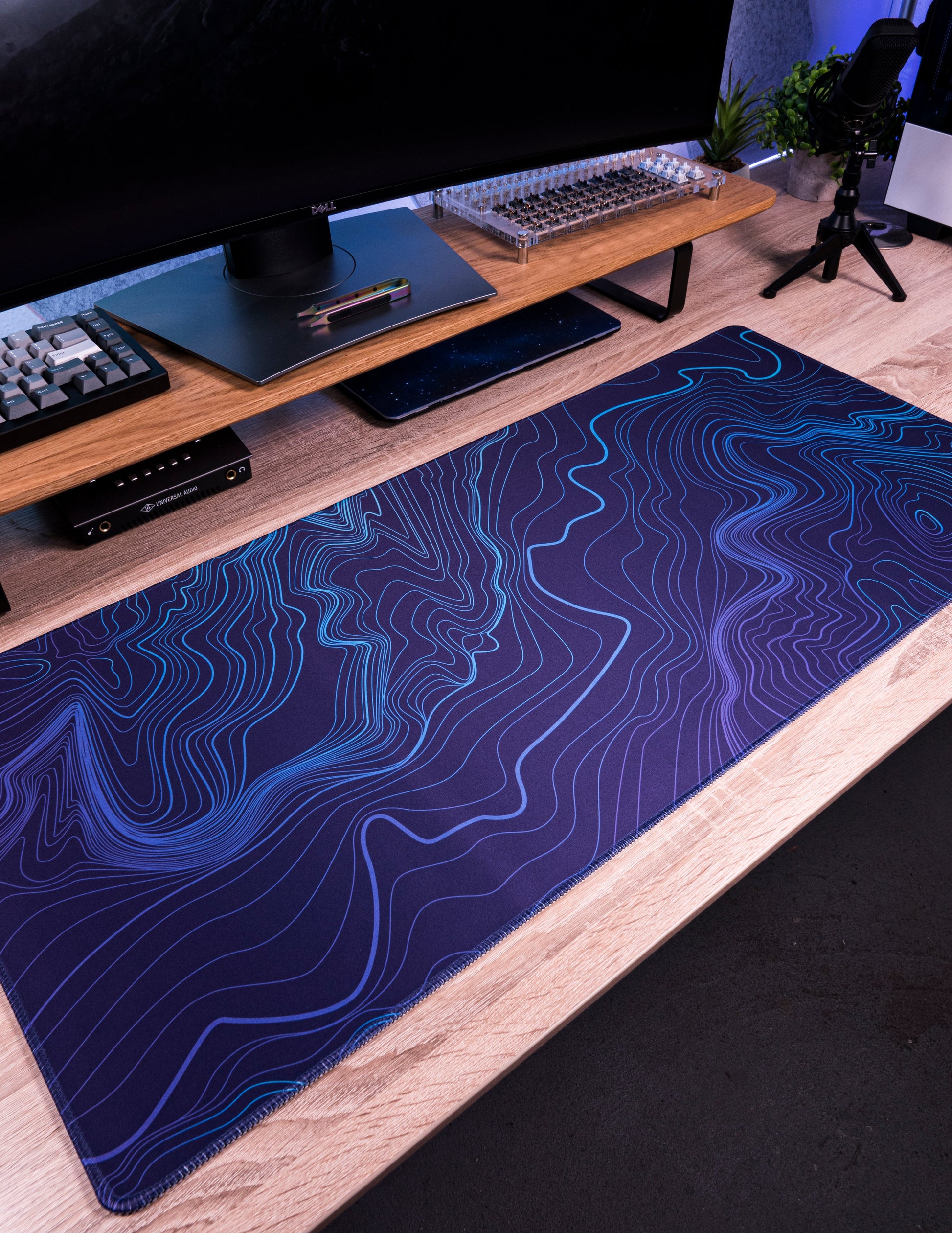 Purple-blue desk mat with blue topographic contour pattern laid on a desk