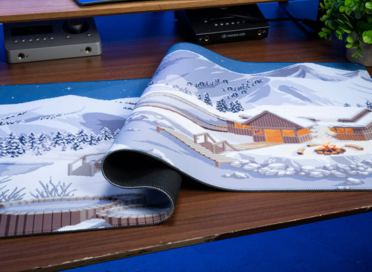 Winter desk mat with mountain village print; rolled edge shows black underside.