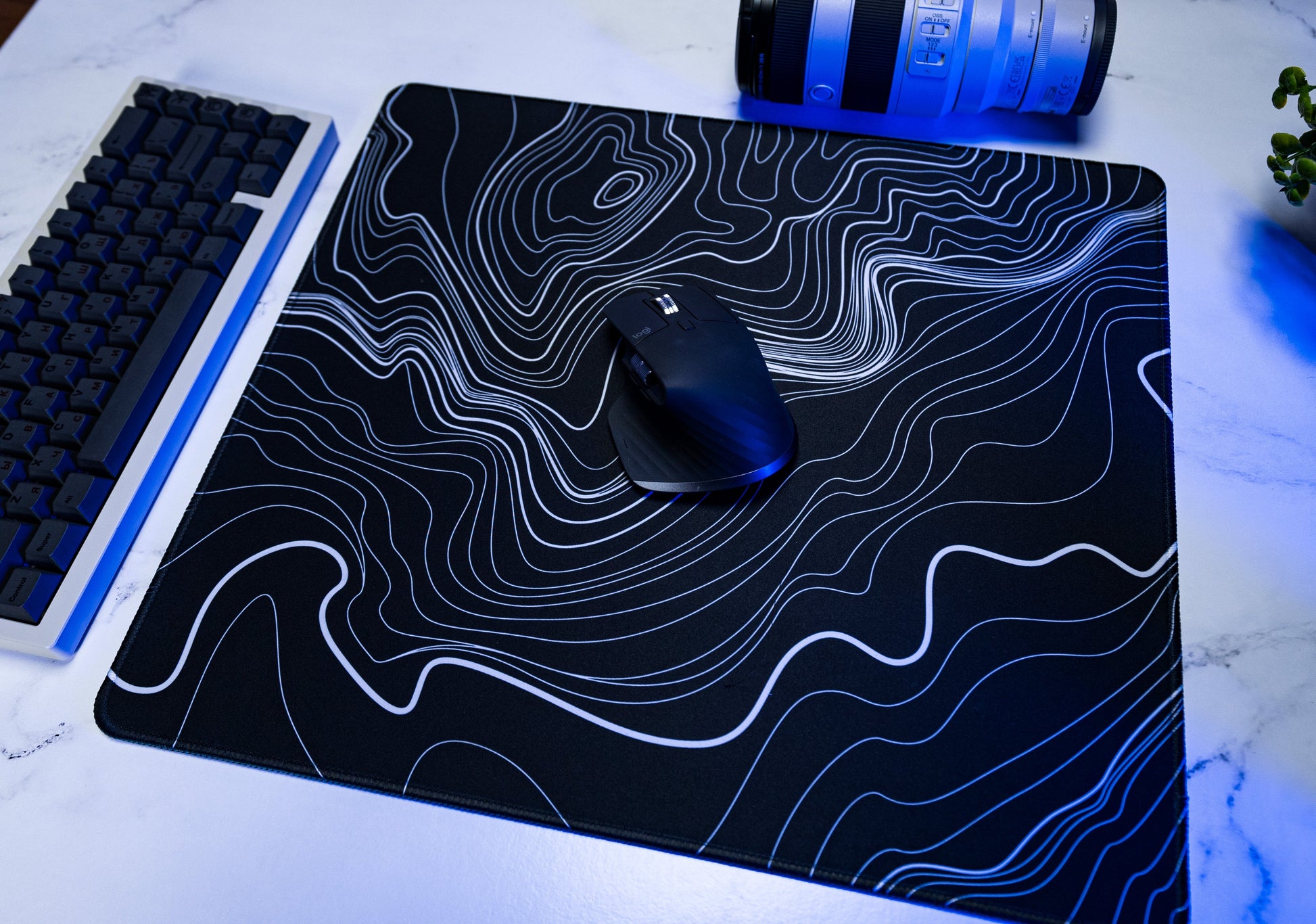 Black desk mat with white topographic line pattern, black mouse near center
