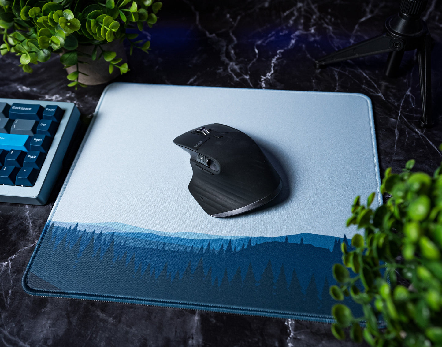 Desk mat with blue forest landscape graphic and zipper-style stitched edge