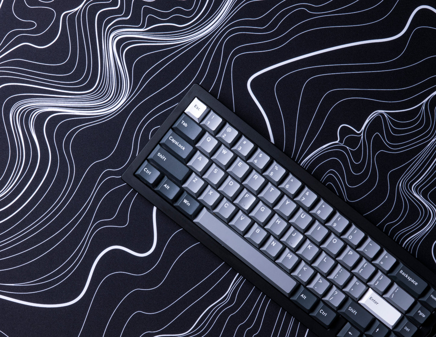 Black desk mat with white topographic line pattern, keyboard lying diagonally