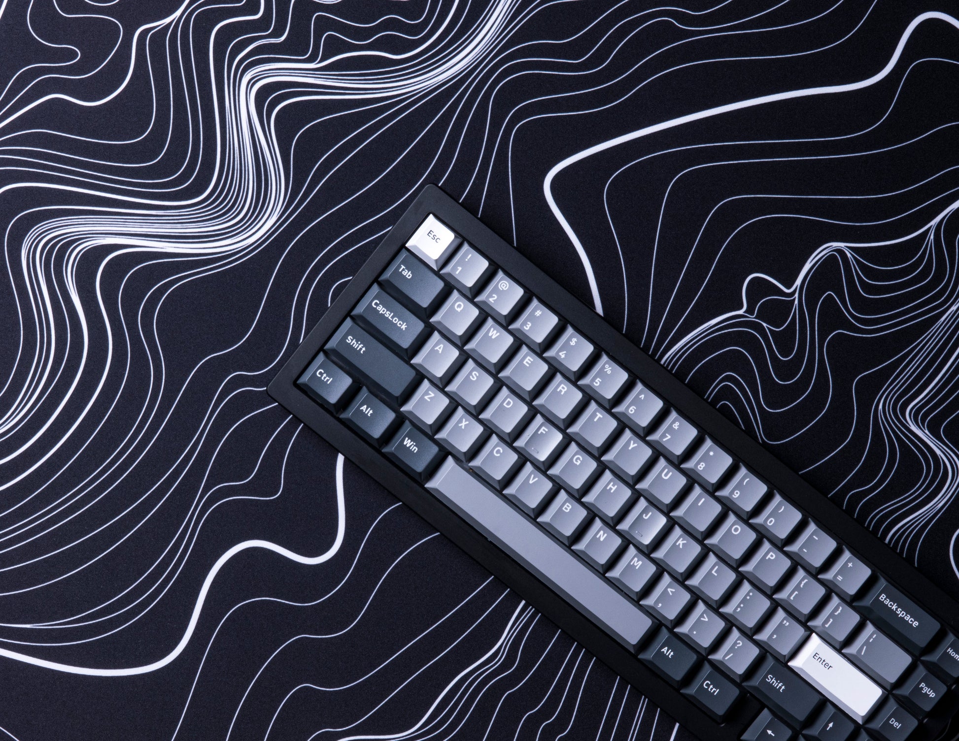Black desk mat with white topographic line pattern, keyboard lying diagonally