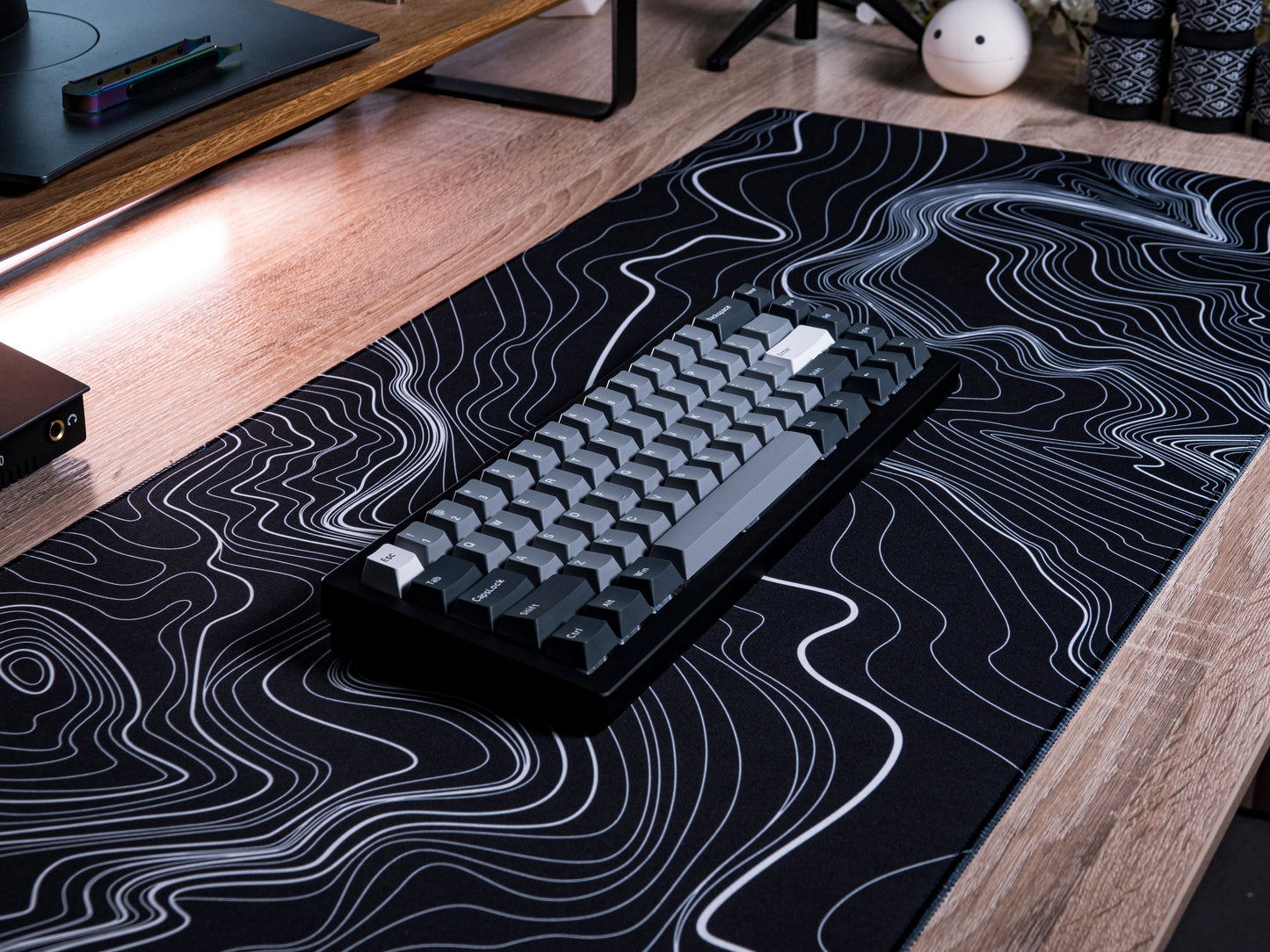 Black desk mat with white topographic line pattern, keyboard centered on top