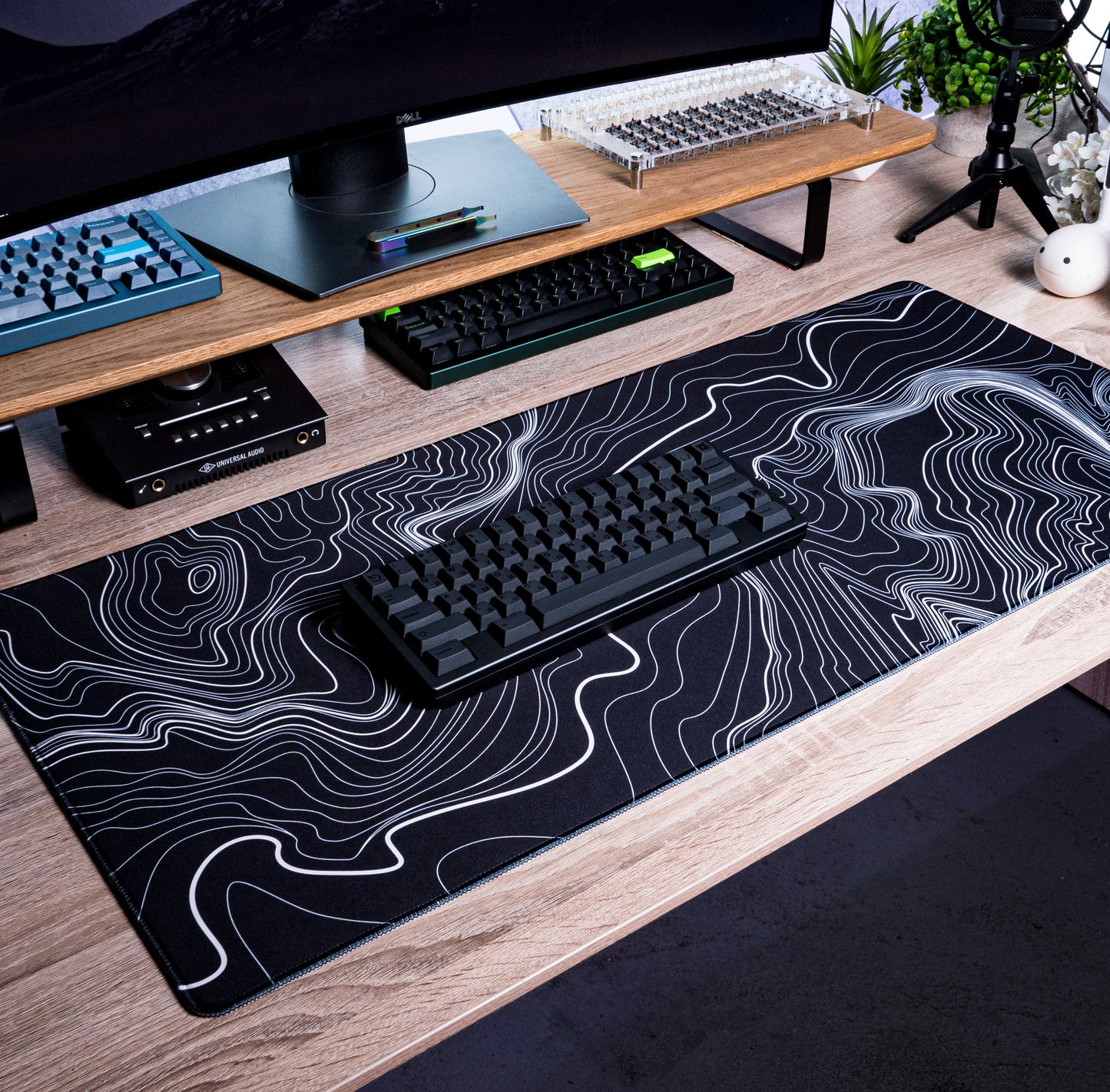 Black desk mat with white contour line topographic pattern under a black keyboard