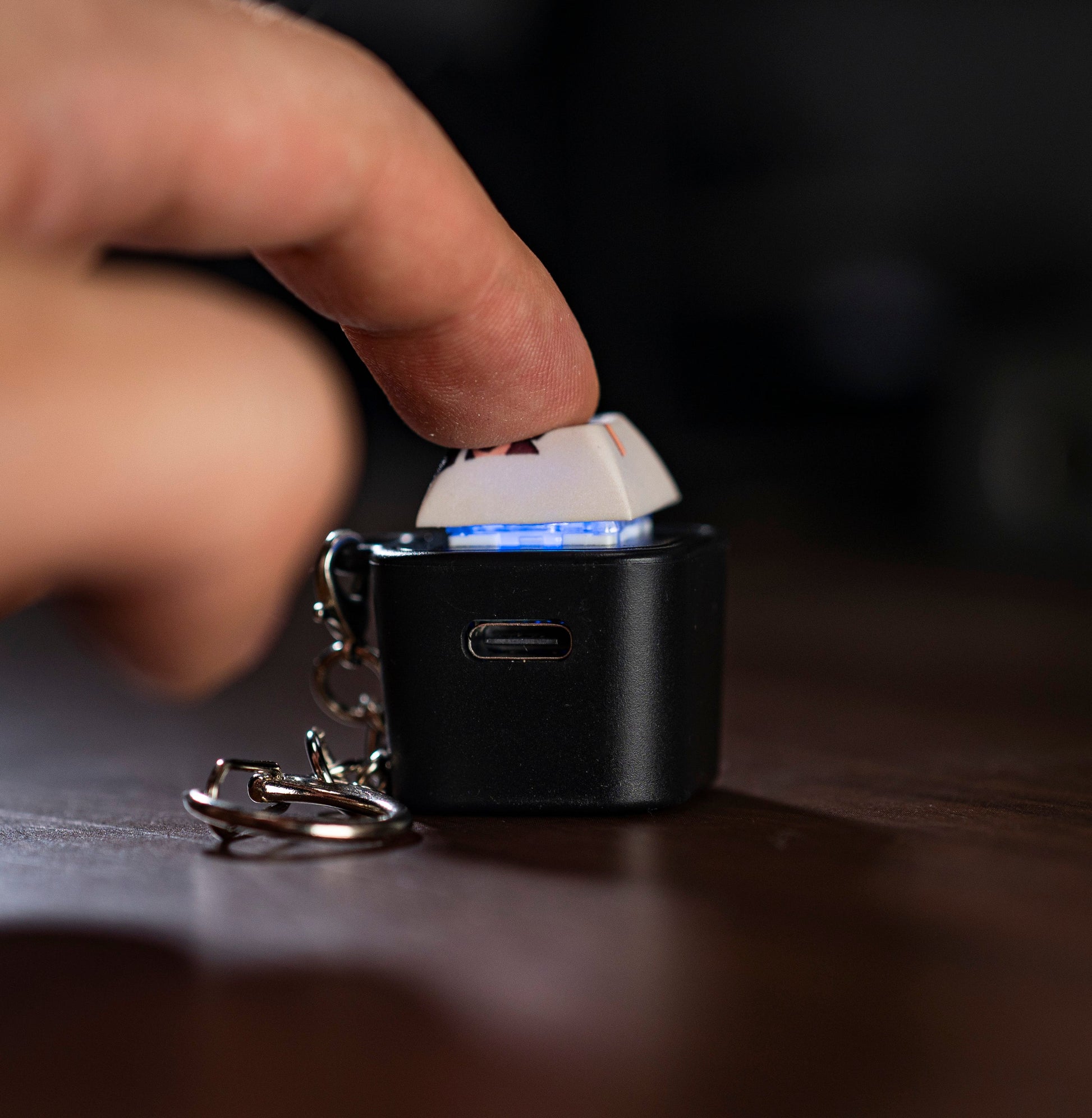 Hand pressing a black keycap animation fidget with blue light on the top