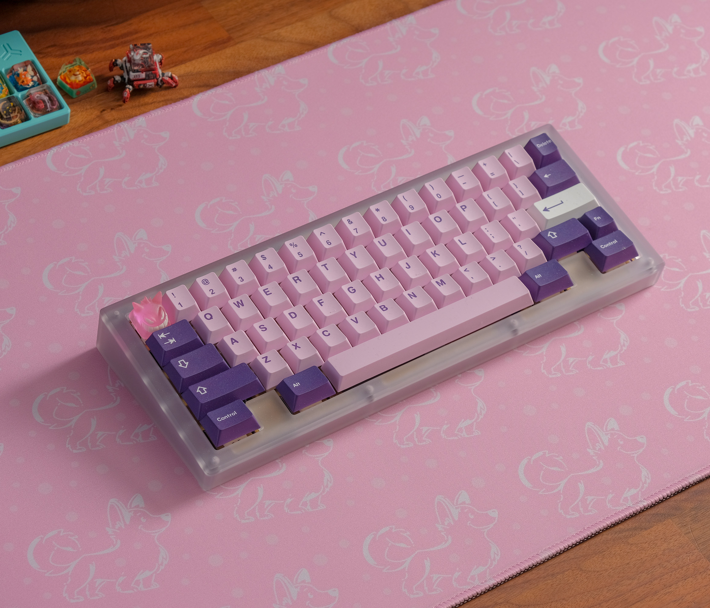 Pink desk mat with white corgi silhouettes and stitched border, keyboard angled on top