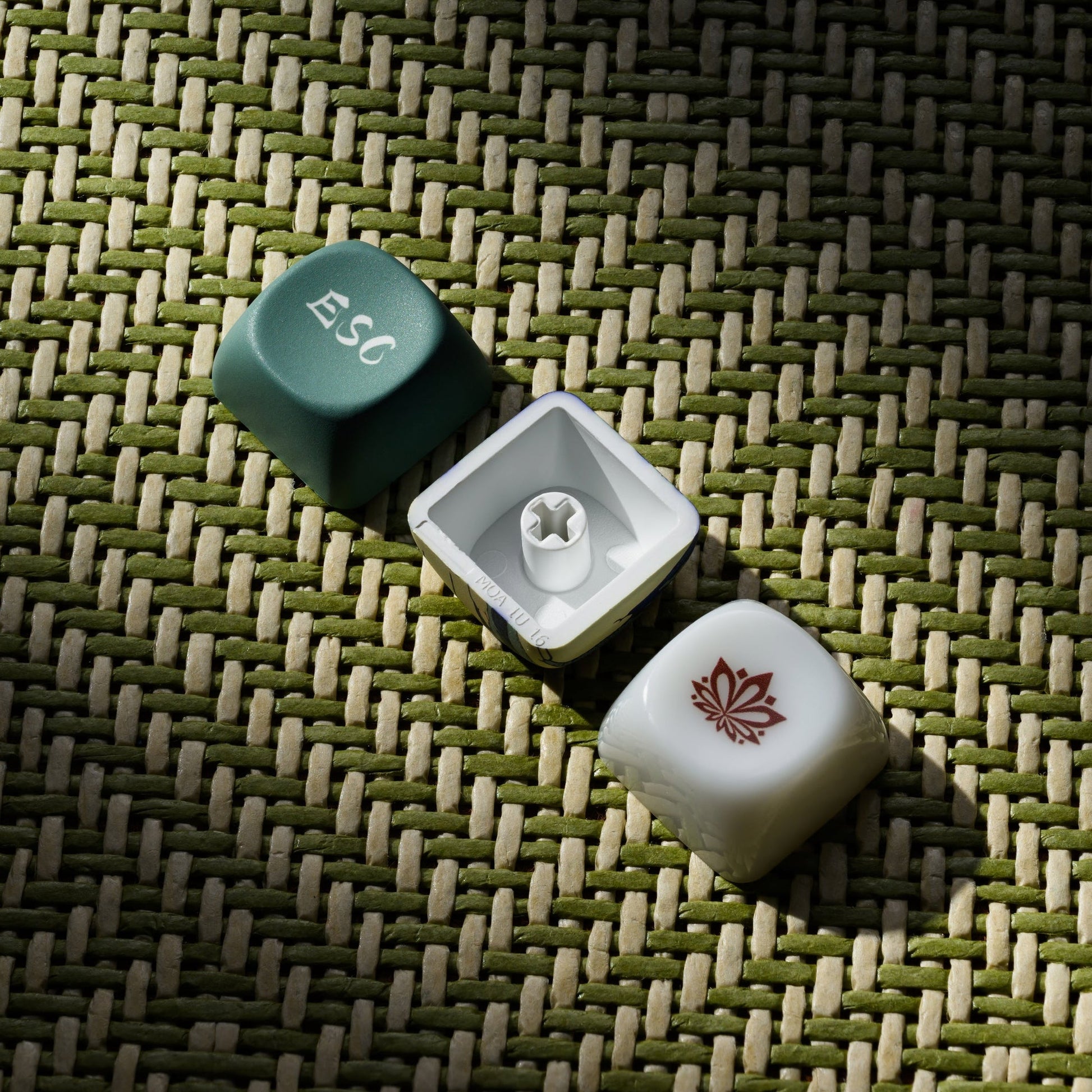 Single keycaps on textured mat: green “Esc” and white modifier with red emblem