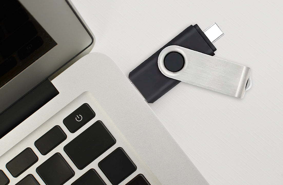 Silver and black dual USB flash drive with circular loop beside a laptop