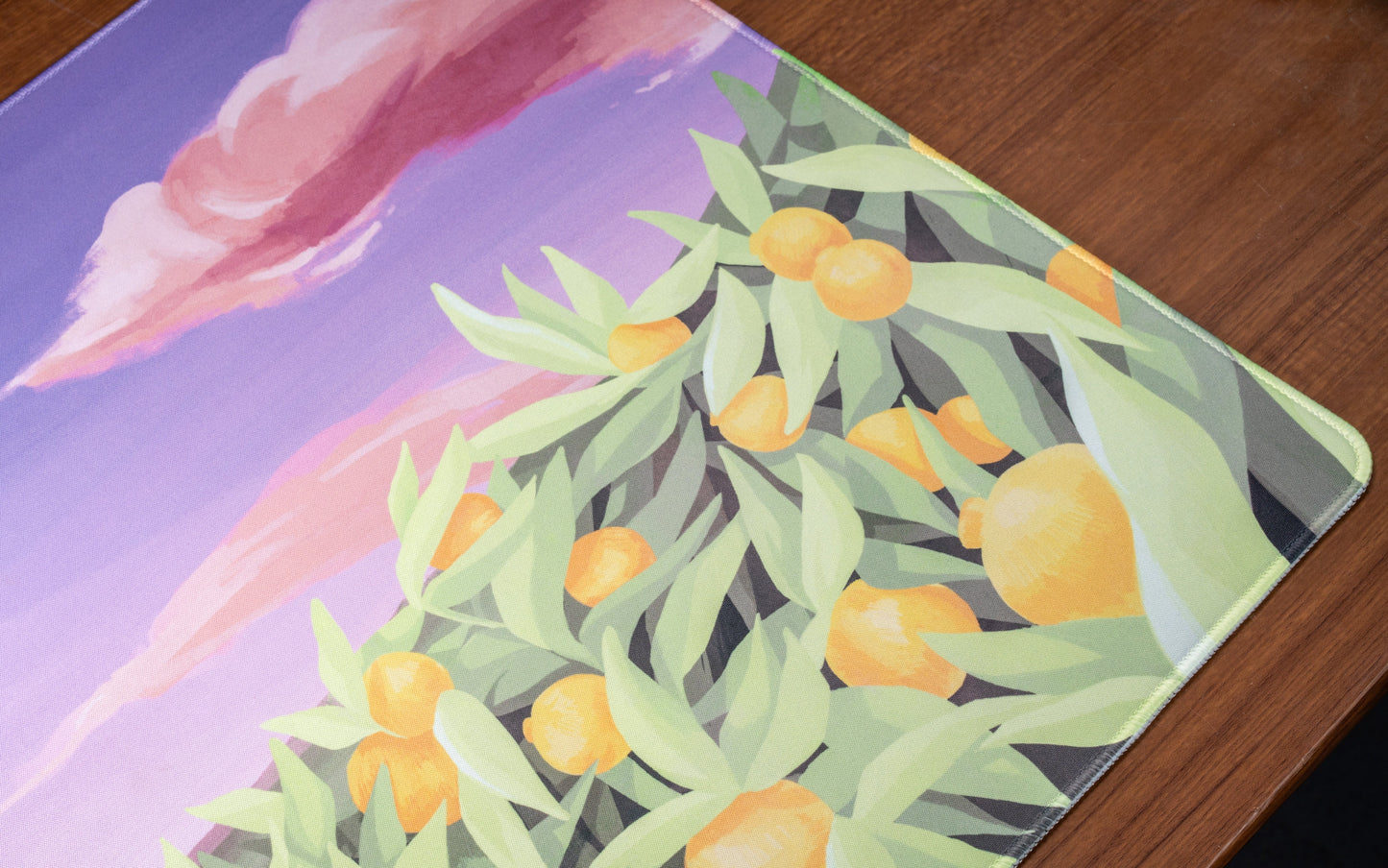 Desk mat close-up of orange citrus and pale green leaves over lavender clouds and hills