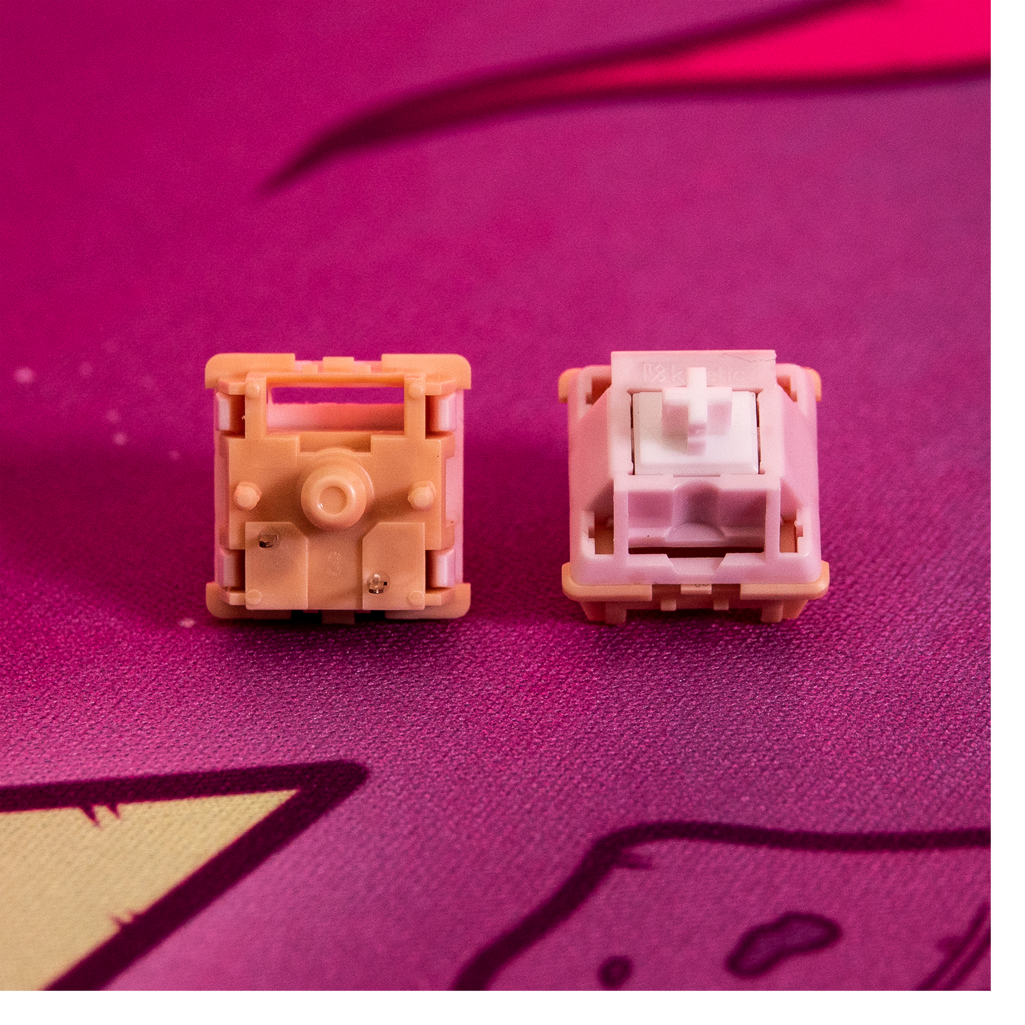 Two Kinetic tactile switches with pink housings and white cross stems on fabric