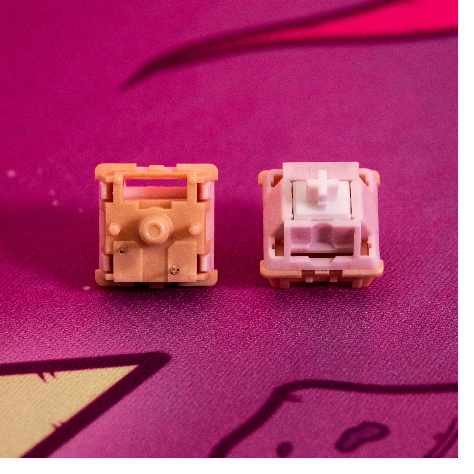 Two Kinetic tactile switches with pink housings and white cross stems on fabric