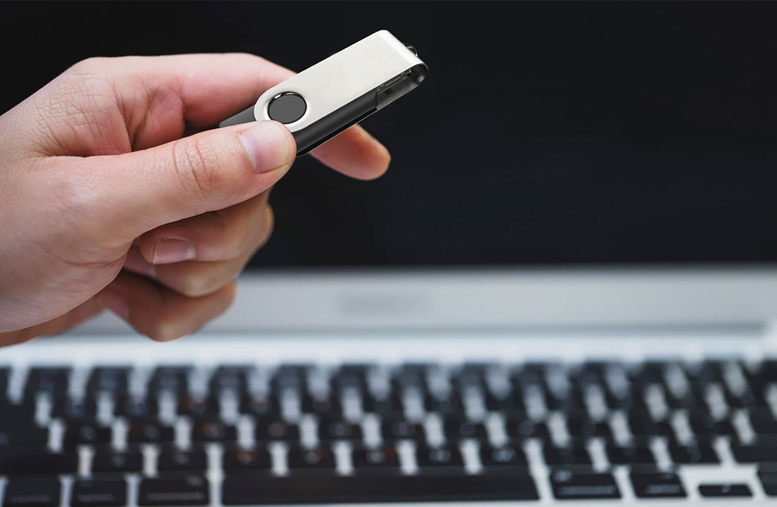 USB 2.0 flash drive held in hand, silver metal body with black swivel cap and ring